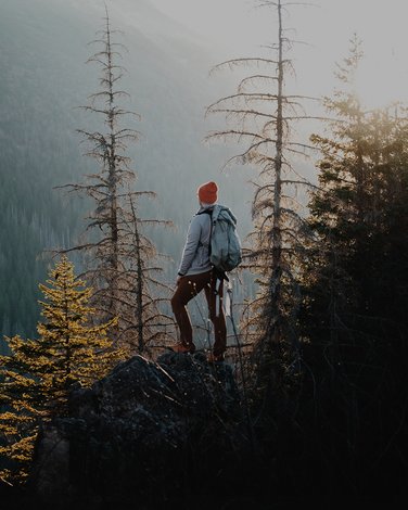 Kobieta w czerwonej czapce, stojąca na szczycie góry, patrząca w dal na widok
