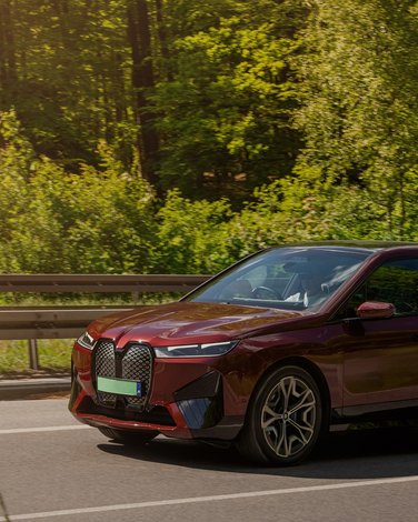 Samochód marki BMW jadący drogą w pięknym zielonym lesie