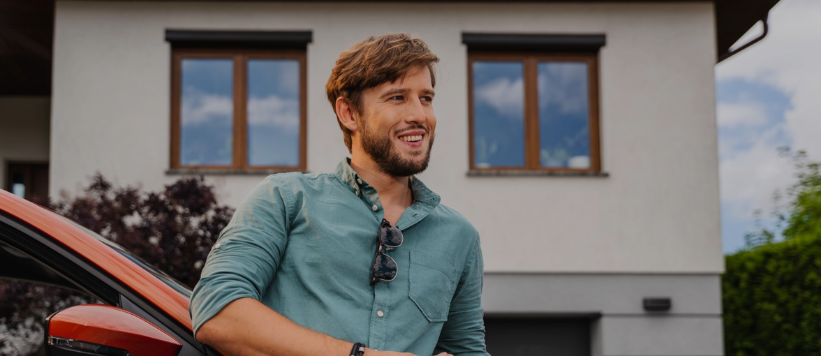 Mężczyzna opierający się na samochodzie w tle dom