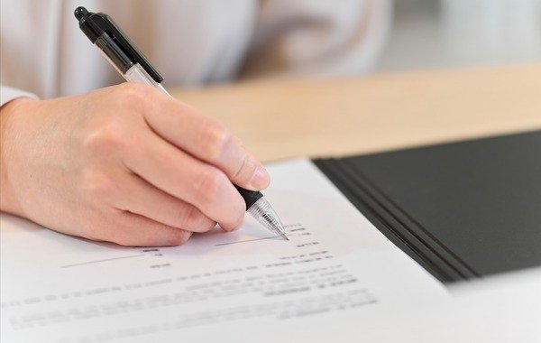 Kobieta podpisująca czarnym długopisem umowę kredytową na biurku.Blog