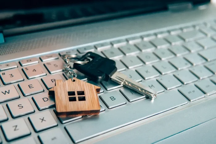 Klucze znajdujące się na klawiaturze laptopa, na kluczach zawieszka obrazująca dom. Blog