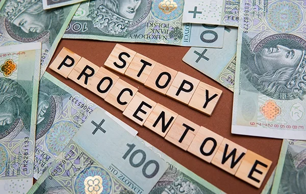 Polskie banknoty rozłożone wokół drewnianych liter układających się w napis "STOPY PROCENTOWE", ilustrujące wpływ stóp procentowych na finanse. Blog.