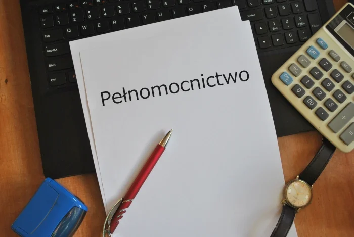 Elementy znajdujące się na biurku: kartka z napisem "pełnomocnictwo", długopis, zegarek, kalkulator, pieczątka, klawiatura. Blog