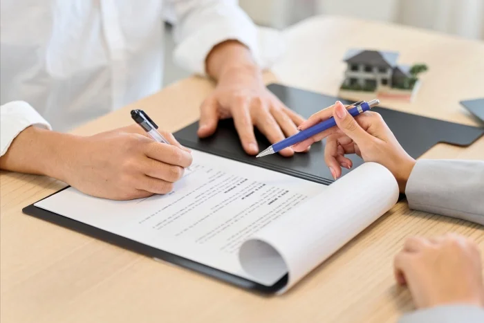 Dłonie znajdujące się nad dokumentem: jedna osoba podpisuje dokument, druga osoba wskazuje obszary do podpisu. Blog