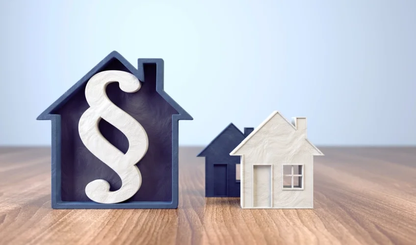 Trzy drewniane dekoracje przedstawiające domki jednorodzinne na drewnianym stole - pierwszy z symbolem paragrafu. Blog