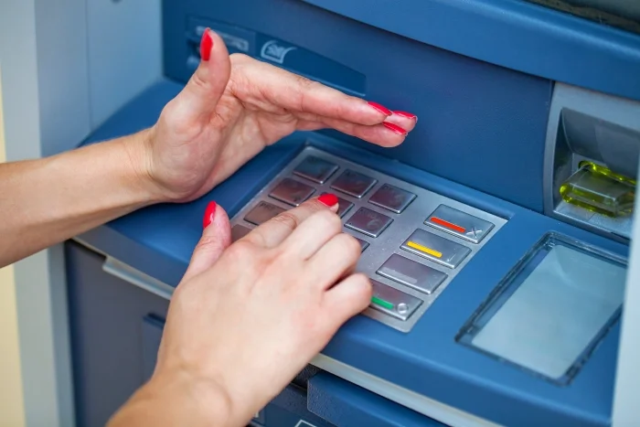Dłoń kobiety wpisująca kod do bankomatu, druga dłoń zasłania klawiaturę. Blog