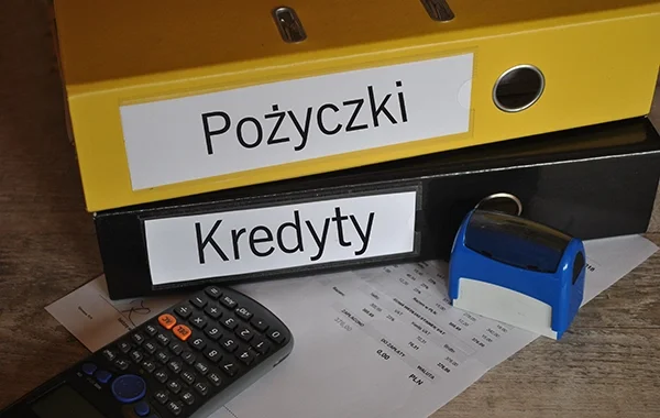 Biurko z segregatorami oznaczonymi "Pożyczki" i "Kredyty", kalkulatorem i pieczątką - elementy istotne przy analizie umowy pożyczki. Blog.