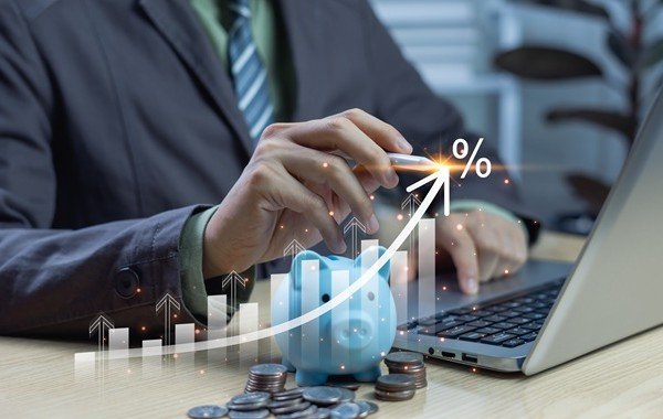 Osoba pracuje przy laptopie, na tle wykres rosnącego oprocentowania i symbol procentu. Blog.